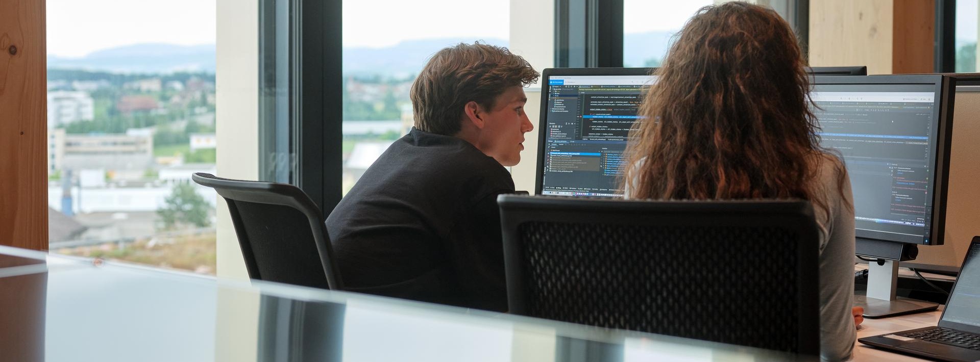 Two coworkers reviewing code on a computer screen in an office